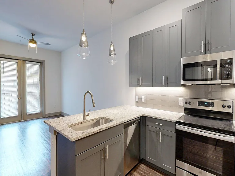 Apartment Kitchen with Stainless Steel Appliances, Dining and Living Room with Wood Style Flooring.