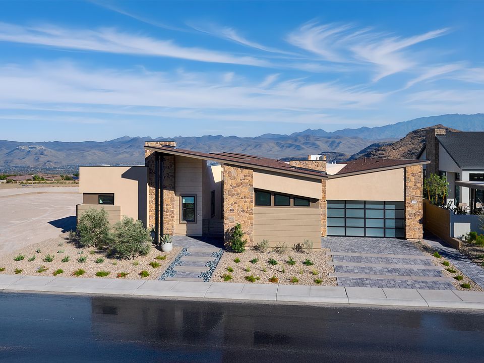 A modern, two-story house with a stone and stucco exterior, surrounded by a paved driveway and lands