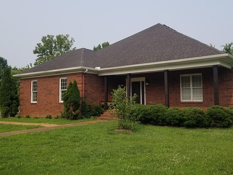 This is the front of the home. It is a dark red brick with stained front door and two sidelites. The bench visible in this picture can stay.