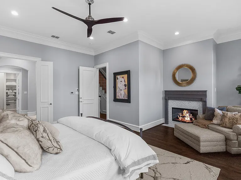 The 3rd-floor is dedicated to the primary suite with tall windows, soft gray walls, dark wood floors, an indoor fireplace, and a neutral-toned bed styled with layered pillows and textured bedding.