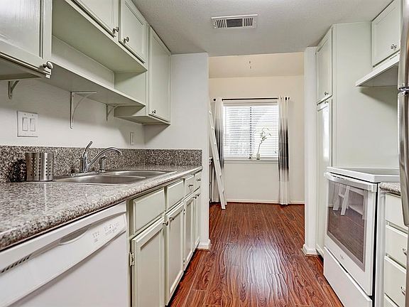 View through the kitchen which features new granite countertops (8/2019), laminate wood floors, dual-bowl stainless steel sink with pull out sprayer and Kenmore dishwasher
