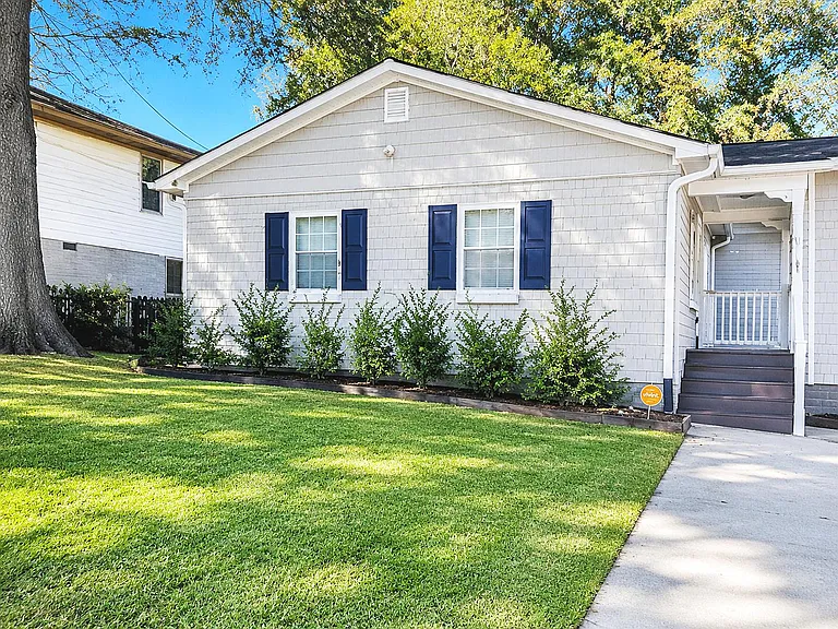 Charming front exterior with a covered entry porch, clean siding, and a well-kept lawn with mature trees.