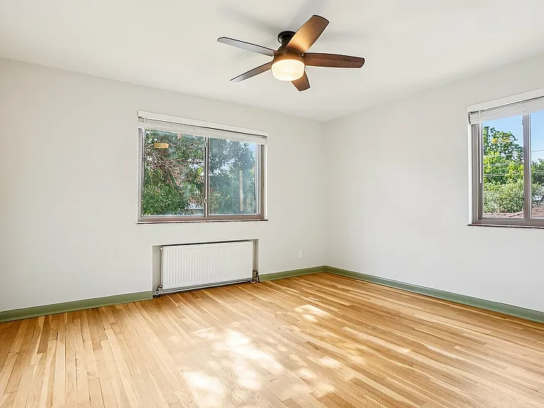 Bright and airy room with polished hardwood floors, large windows offering scenic views, and a modern ceiling fan.