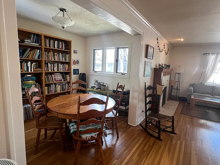 April 2026-Dining area with matching large windows on left and right. Original wood flooring throughout. Bookcases and table and chairs remain with the house.