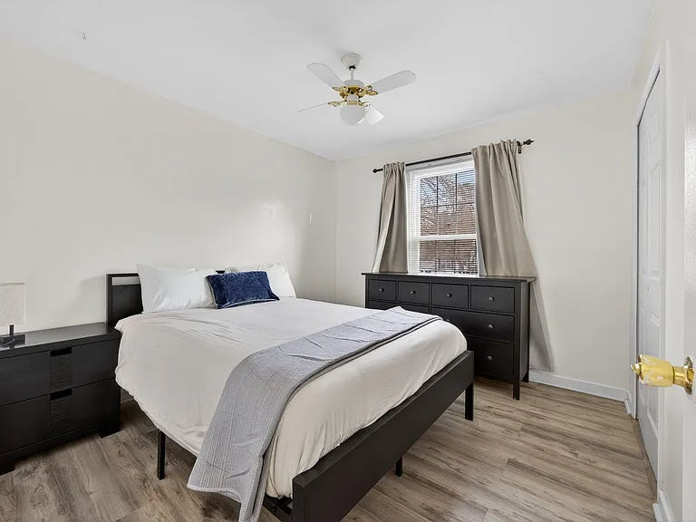Furnished bedroom with a full bed, dresser, and nightstand, plus a window with curtains and a ceiling fan for comfort.