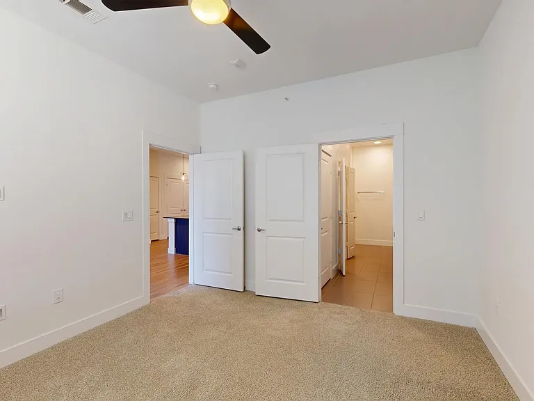 Spacious apartment bedroom with large closet, attached bathroom, and plush carpet flooring.