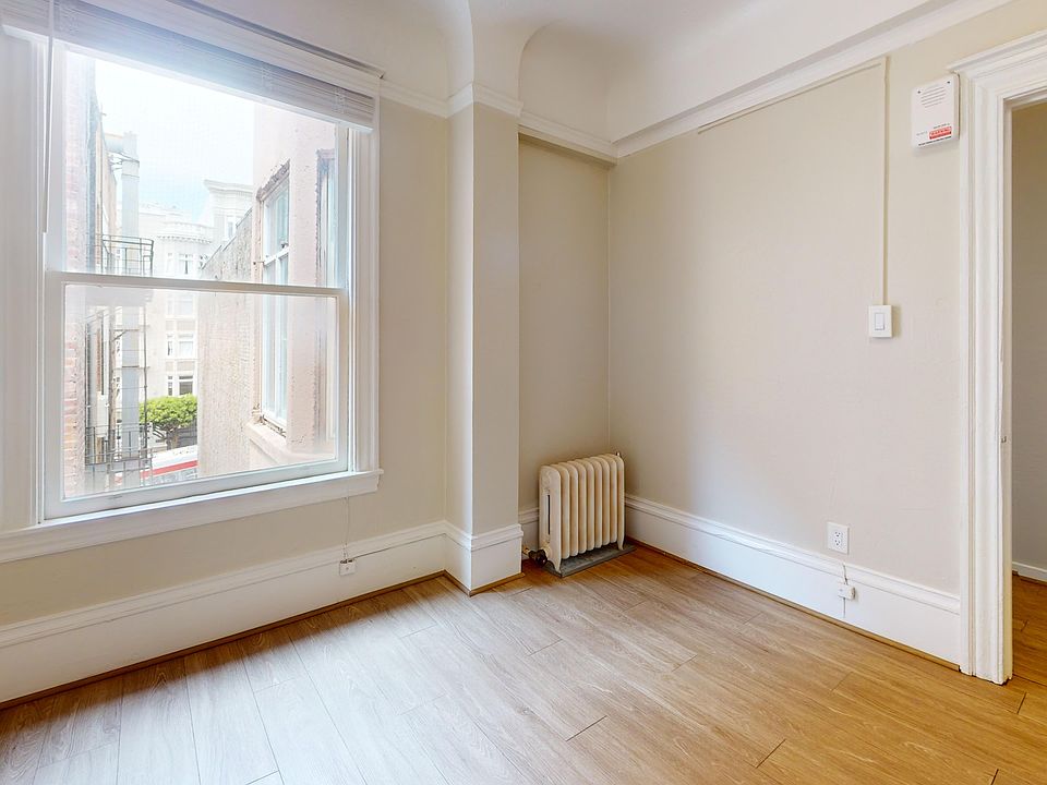 Bright corner of a room featuring a large window, wood flooring, and a vintage radiator against walls.
