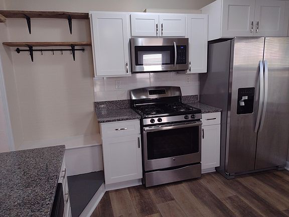 Granite countertop, white cabinetry, rustic wood shelving