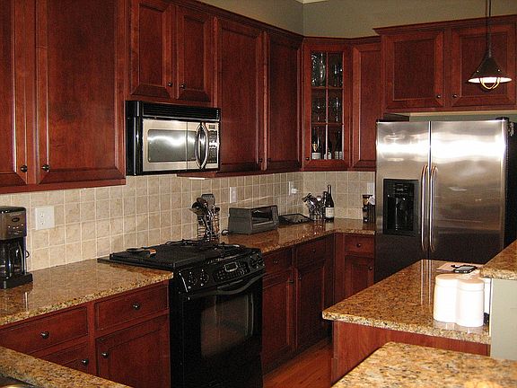 Gourment kitchen featuring granite countertops, stainless steel appliances, cherry cabinets, tile backsplash, wrap-around bar, and island.