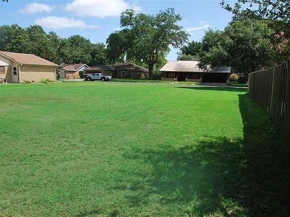 A lot with lush grass on a street with lovely trees.