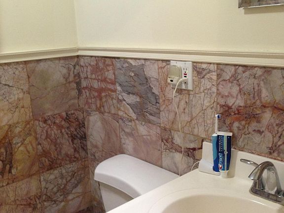 Bathroom has marble floors and walls Full bathtub with shower Sink with cabinet underneath Medicine cabinet above sink