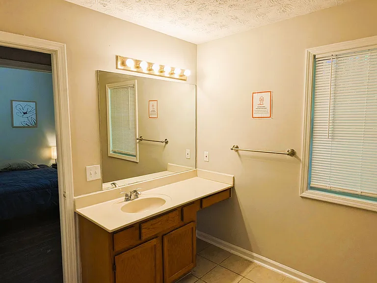 Bathroom vanity area with a wide countertop, oversized mirror, and under-sink storage plus a window for ventilation.
