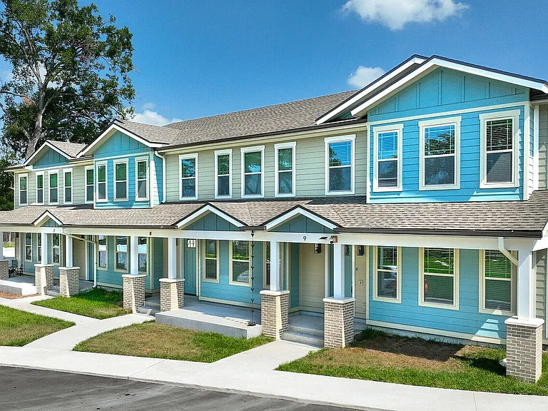 Charming townhouse with vibrant blue siding, featuring modern architecture, large windows, and neatly landscaped lawns.