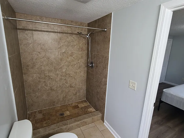 Walk-in tile shower with handheld showerhead and matching tile flooring, located just off the adjacent bedroom.