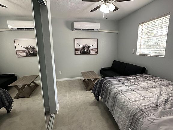 Furnished bedroom with tiled floors, mirrored closet doors, ceiling fan, window blinds, and a wall-mounted mini-split AC.