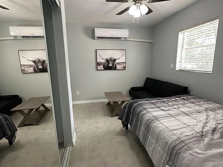 Furnished bedroom with tiled floors, mirrored closet doors, ceiling fan, window blinds, and a wall-mounted mini-split AC.