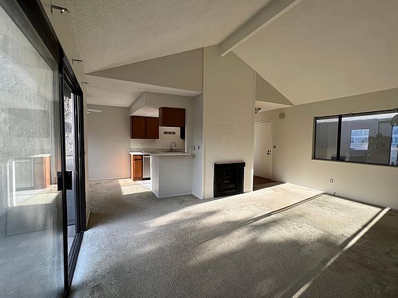 Living room with fireplace and vaulted ceiling. Sliding glass door at left leads to balcony. Front door to the right of fireplace.