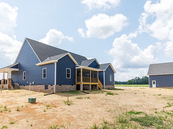 New blue house with covered porch and detached garage on a barren, dirt-filled lot under a partly cl