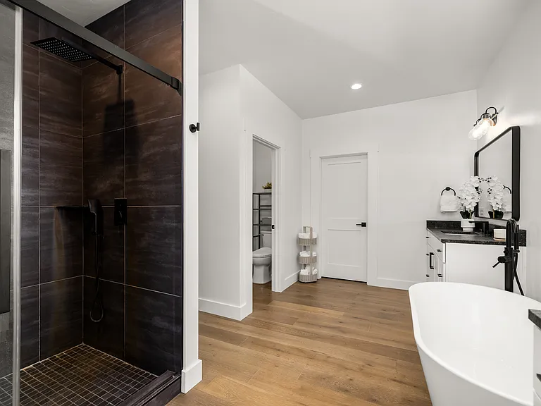 Luxurious spa-style en-suite featuring an oversized walk-in shower with dramatic black finishes, sleek modern fixtures, elegant designer touches, and a refined mountain-modern feel throughout.