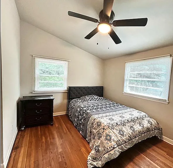 Bedroom with hardwood floors, two windows with blinds, ceiling fan, and space for a bed plus a dresser or desk.