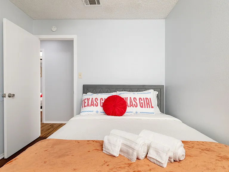 This inviting second bedroom features a queen bed with playful "Texas Girl" pillows and a warm orange throw.