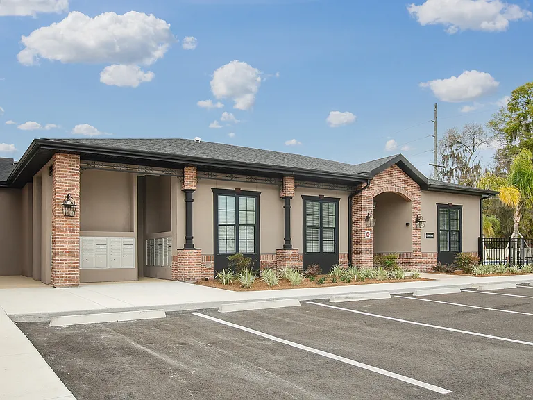 Charming apartment complex entrance with elegant brick accents and well-maintained landscaping under a bright blue sky.