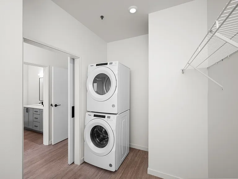 Modern apartment laundry area with stacked washer and dryer, adjacent to a sleek bathroom featuring stylish cabinetry. Modern apartment laundry area with stacked washer and dryer, adjacent to a sleek bathroom featuring stylish cabinetry.