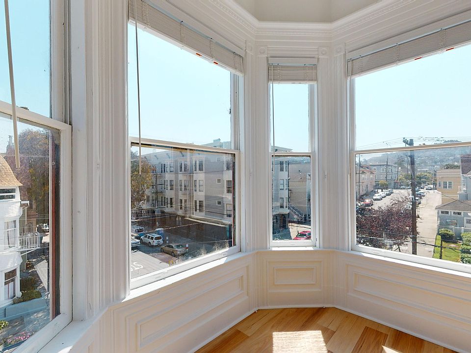 Well-lit room with a large window offering a view of the city skyline, with a wooden floor