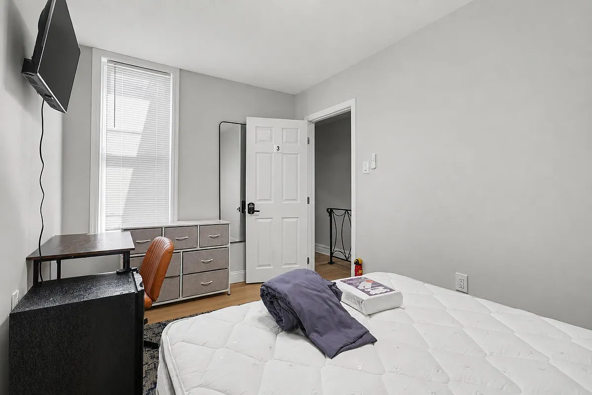 Private bedroom with hardwood floors, a large window with blinds, dresser storage, desk workspace, and wall-mounted TV. - N 28th St