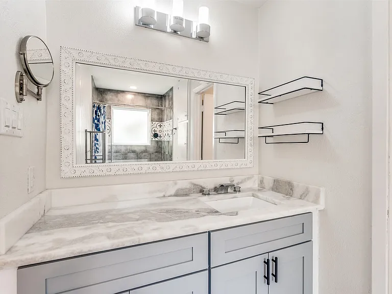 Bathroom vanity featuring a light gray cabinet with dark hardware, a white undermount sink, and a stone-finish countertop