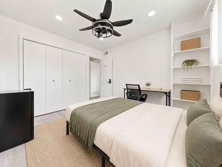 Well-appointed bedroom with a ceiling fan, large closet, built-in shelving, and a dedicated desk workspace.