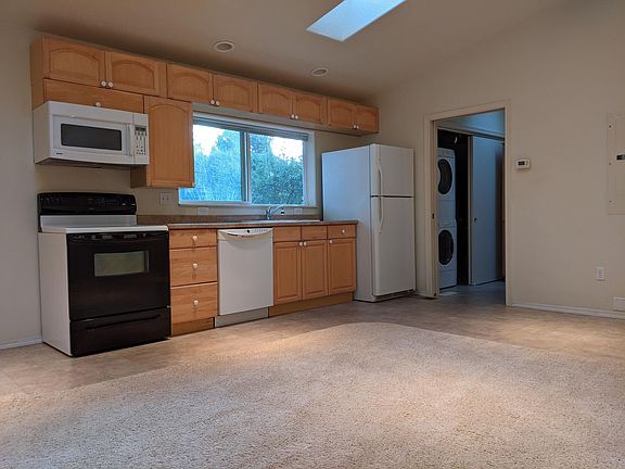 Combined living room and kitchen showing glass-top stove, dishwasher, microwave and refrigerator.
