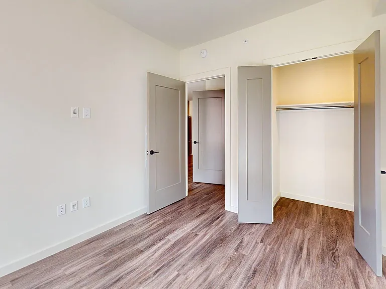 Spacious apartment bedroom with large closet and wood-style flooring.