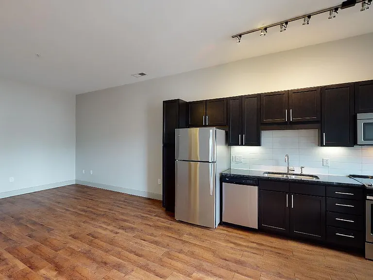 Apartment kitchen with stainless steel appliances, granite countertops and wood-style flooring.