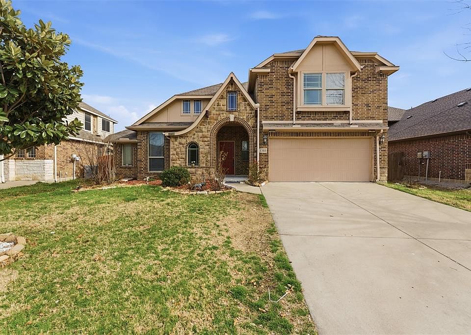 Tudor home featuring brick siding, an attached garage, concrete driveway, and a front yard