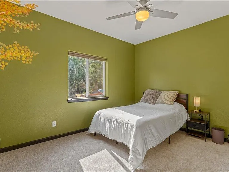 Bedroom with green accent walls, carpeted floors, a large window, and a ceiling fan with light for year-round comfort.