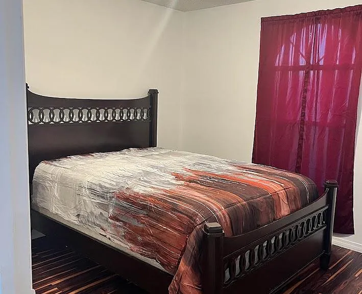 Furnished bedroom with a full-size bed, overhead lighting, and easy-care flooring plus a window with curtains.