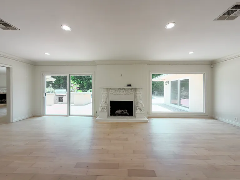 Symmetrical sliding glass doors flank the fireplace in this bright living room within a Beverly Hills luxury rental at 1094 Garden Lane, a 90210 home for rent.