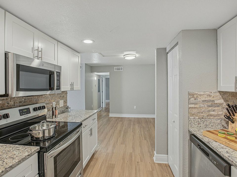 Modern kitchen with sleek stainless steel appliances, granite countertops, and stylish cabinetry opening into a bright hallway.