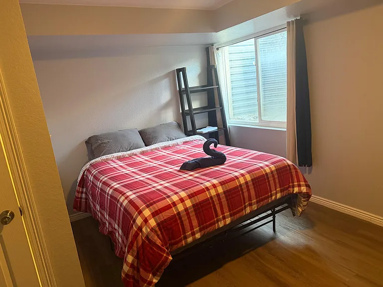 Furnished bedroom with a full-size bed, bedside shelving, and a large window with curtains for natural light and privacy.