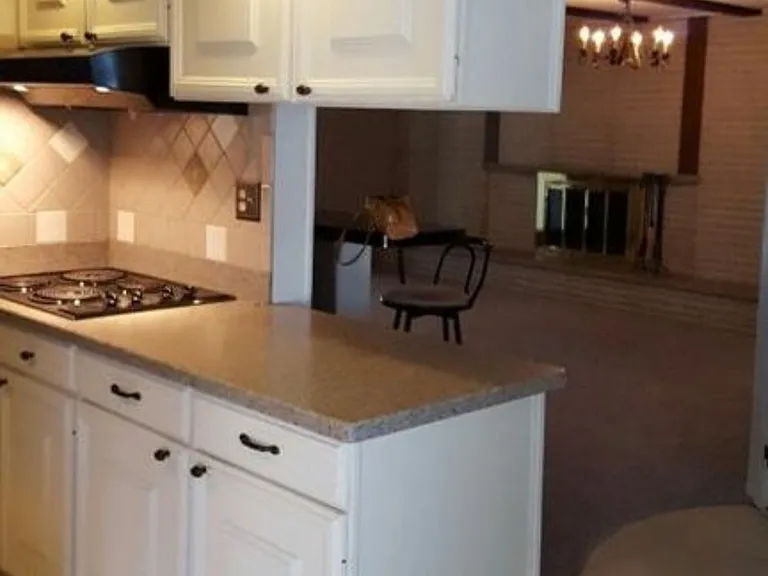 Kitchen, looking past bar area with two bar stools into family room (door to right of picture to enter garage). Cooking area to the far left in kitchen.