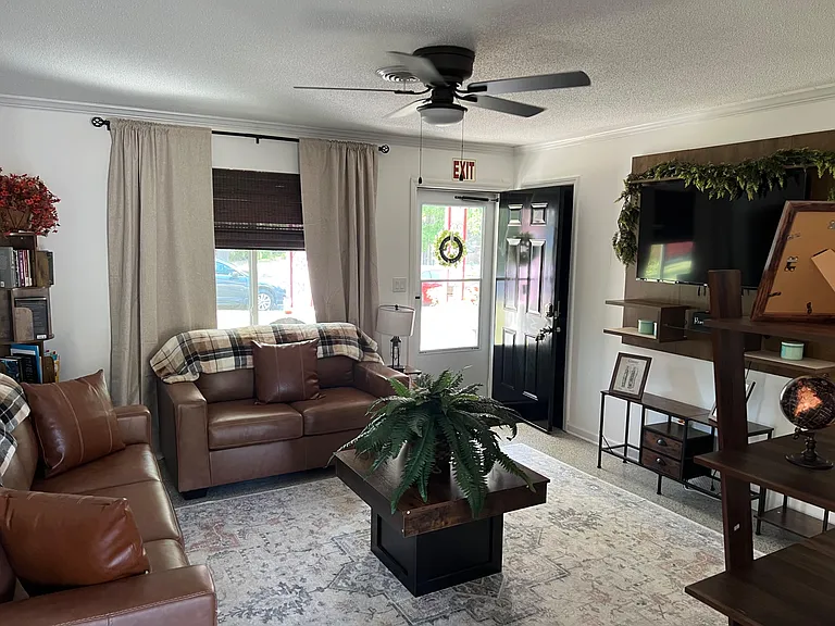 Living room with leather seating, large TV wall unit, and front entry with nearby windows for daylight.