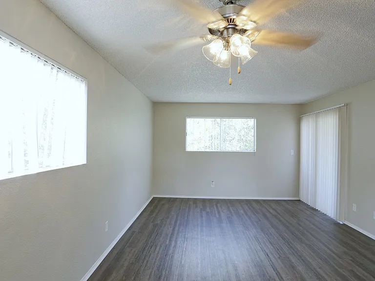 Dining araa with ceiling fan and living room with plank style flooring and lots of windows for natural light at Villa Pacific Apartments in Oceanside, California.