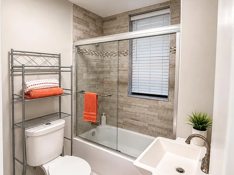 Updated full bath with a tiled tub/shower, sliding glass doors, vanity sink, and a window for ventilation and light.