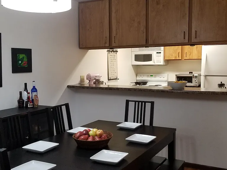 Another view of dining area, facing a kitchen with pass-through serving and high cabinets.