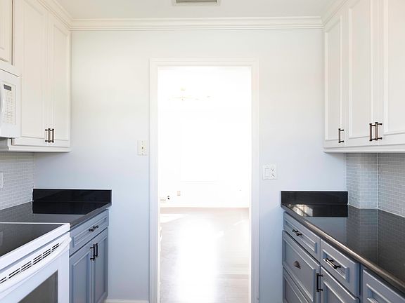Full-sized galley kitchen with tile backsplash, granite countertop, custom wood cabinetry and full-size appliances, looking into living room