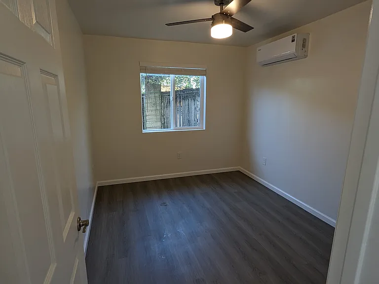 Bright bedroom with private deck access, sleek hardwood-style floors, and a modern ceiling fan. Includes a dedicated heat pump for personalized AC/heating and a full-size closet. Perfect for indoor-outdoor living and year-round comfort.