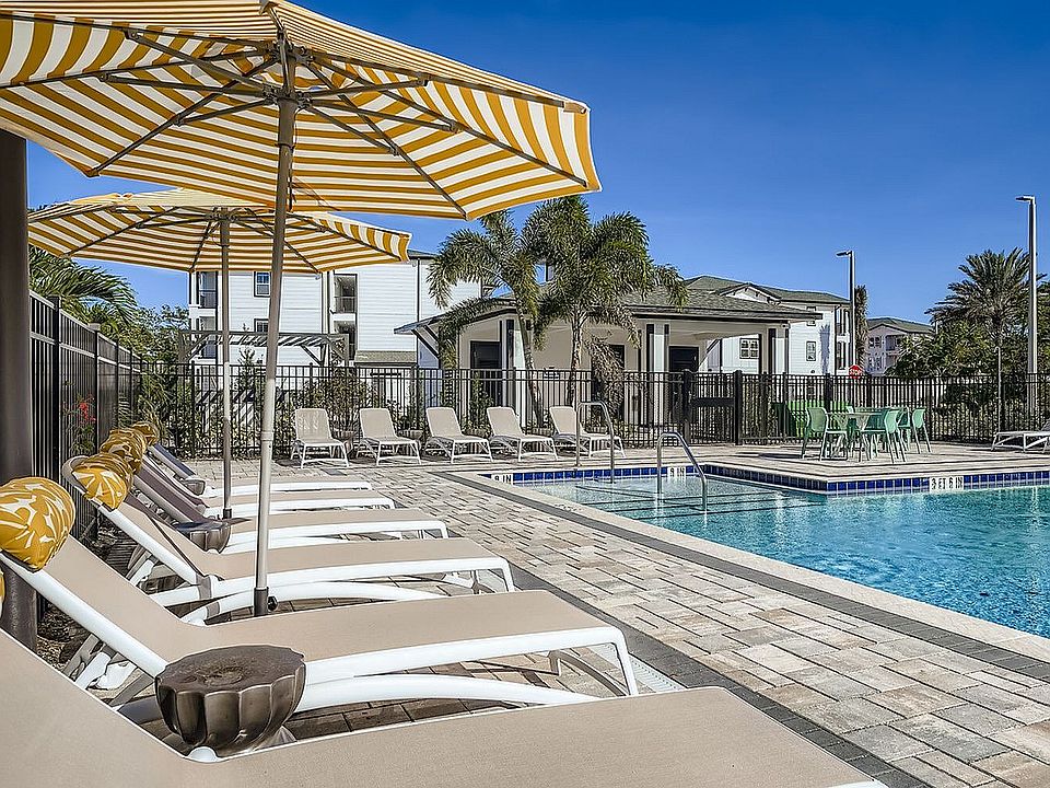 Premium outdoor pool area with elegant sun loungers, striped umbrellas, and lush greenery, perfect for relaxation and leisure.