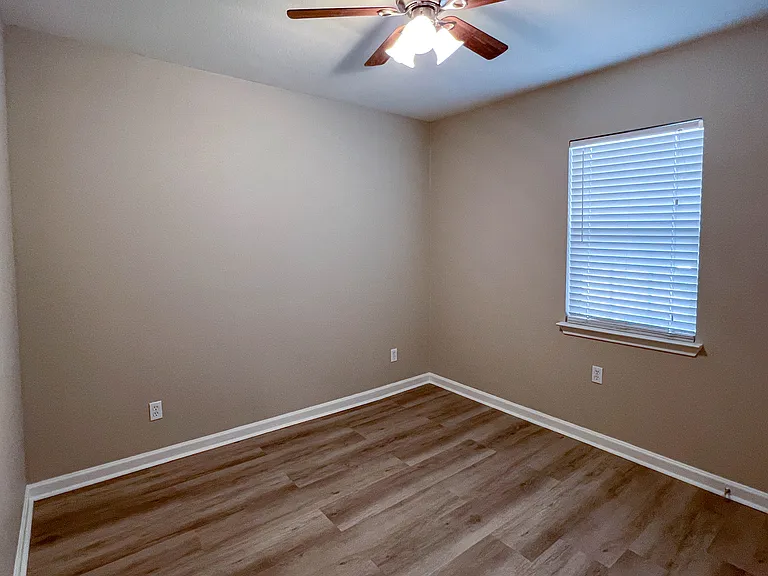 Spacious secondary bedroom with wood-look flooring, a ceiling fan, and natural light.