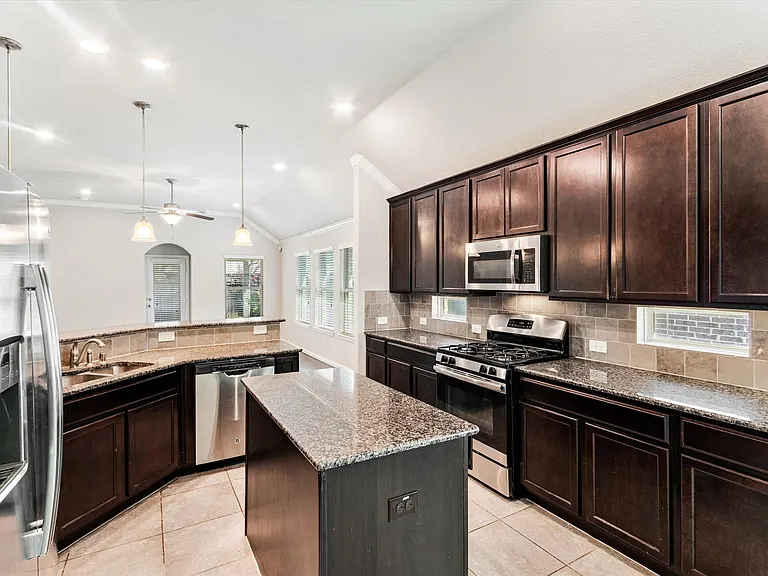 Kitchen featuring dark wood cabinetry, granite countertops, tile flooring, stainless steel appliances, and a central island